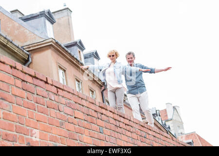 Low angle view of middle-aged woman with arms outstretched marcher sur mur de brique contre ciel clair Banque D'Images