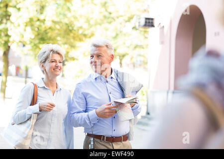 Happy middle-aged couple with map walking in city Banque D'Images