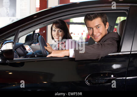 Portrait de jeune couple assis dans une nouvelle voiture à la salle d'exposition Banque D'Images