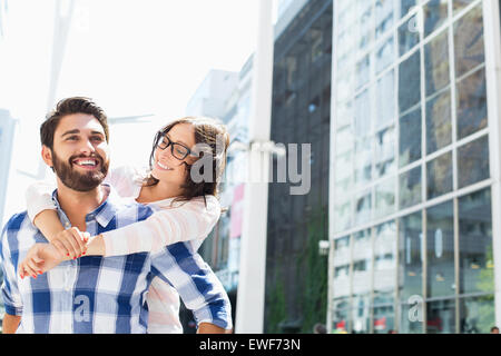 Happy man giving piggyback ride to woman in city Banque D'Images
