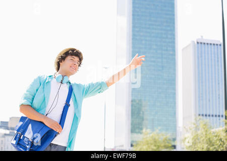 Jeune homme souriant saluant un taxi en ville Banque D'Images