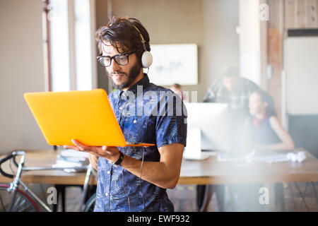 Businessman wearing headphones and using laptop in office Banque D'Images
