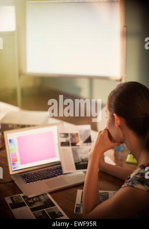 L'accent creative businesswoman working at laptop et l'examen de photographies Banque D'Images