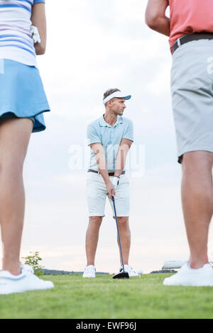 Man playing golf contre ciel avec friends standing in foreground Banque D'Images