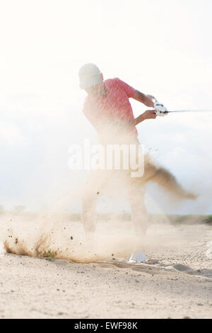 Homme d'âge moyen splashing sand tout en jouant au golf Banque D'Images