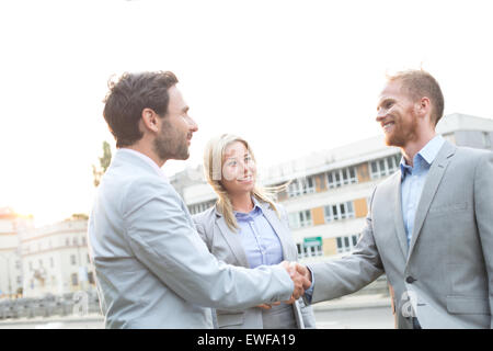 Happy businessmen shaking hands in ville contre un ciel clair Banque D'Images