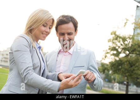 Happy business couple using smart phone at park Banque D'Images