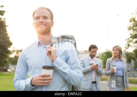 Happy businessman holding disposable cup avec des collègues debout en arrière-plan Banque D'Images