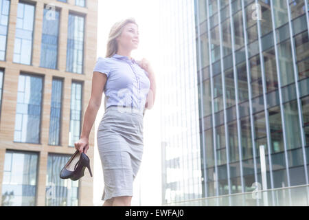 Low angle view of confident businesswoman holding High heels, les édifices à bureaux Banque D'Images