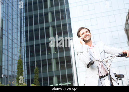 Low angle view of businessman answering mobile phone while sitting on bicycle outdoors Banque D'Images