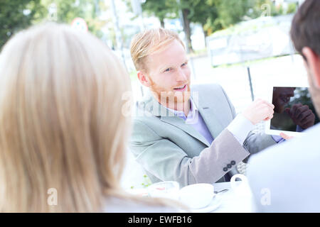 Businessman discussing over digital tablet avec des collègues at sidewalk cafe Banque D'Images