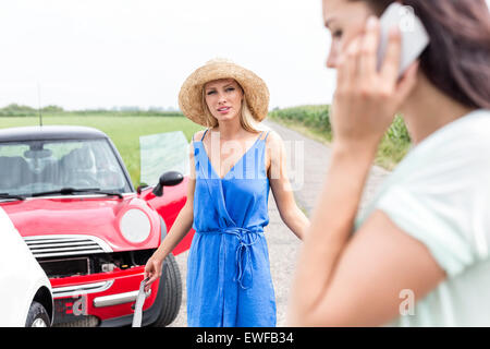 Femme en colère à la femelle à l'aide de téléphone cellulaire par voitures endommagées sur route Banque D'Images
