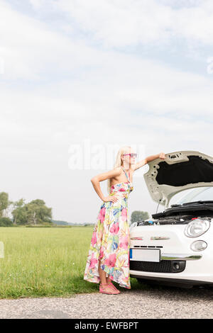 De toute la longueur tendue woman standing by broken down car on country road Banque D'Images