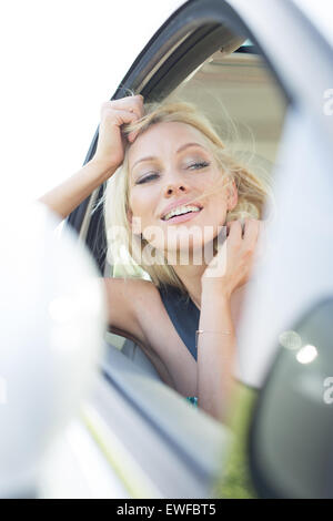 Happy young woman leaning on car window Banque D'Images