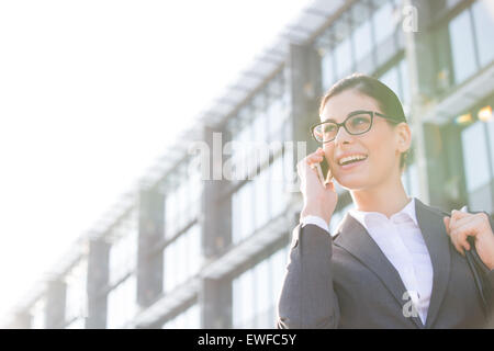 Low angle view of happy businesswoman using cell phone outside office building Banque D'Images