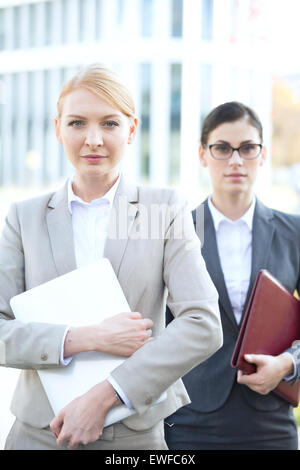 Portrait of businesswoman holding laptop avec collègue en arrière-plan Banque D'Images