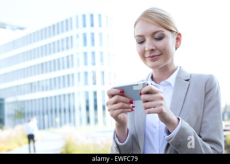 Businesswoman text messaging via smart phone outdoors Banque D'Images