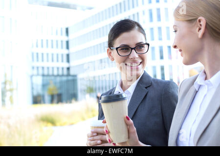 Les femmes d'affaires heureux de converser tout en maintenant des gobelets jetables en plein air Banque D'Images