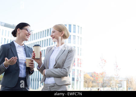 Les femmes d'affaires heureux de converser tout en maintenant des gobelets jetables outside office building Banque D'Images