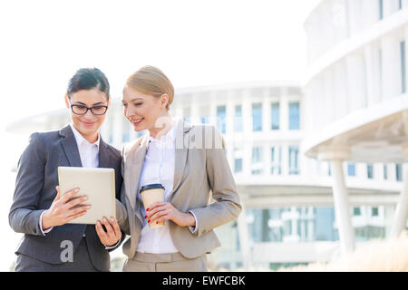 Heureux businesswomen using digital tablet outside office building Banque D'Images