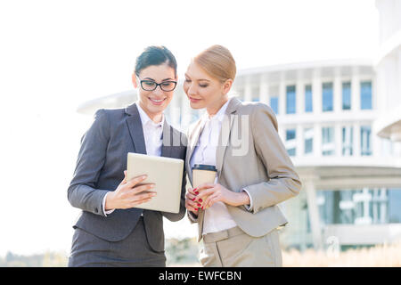 Heureux businesswomen using tablet PC outside office building Banque D'Images