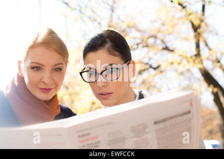 Businesswomen reading newspaper at park Banque D'Images