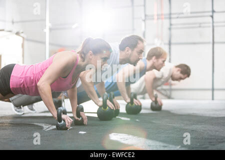 Vue de côté de gens déterminés faisant pompes avec kettlebells à crossfit gym Banque D'Images