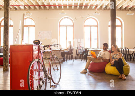 Creative business people using laptop sur des sièges-sacs in office Banque D'Images