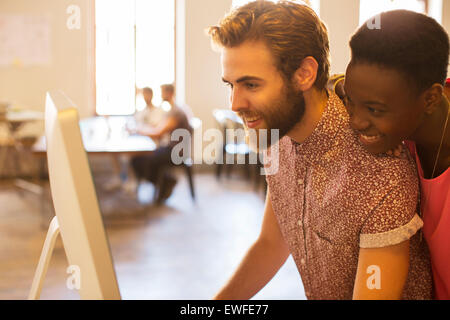 Smiling casual business people sharing computer in office Banque D'Images