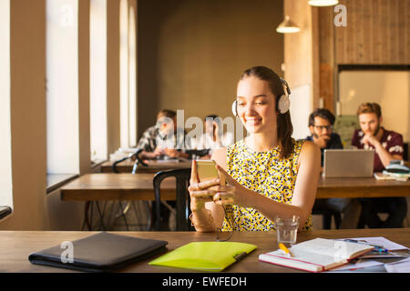 Femme d'occasionnels avec des écouteurs using cell phone in office Banque D'Images