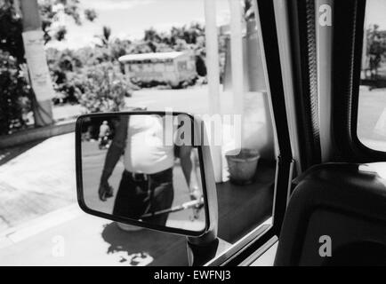 Réflexion d'un préposé de l'essence dans un miroir de l'aile avec un bus abandonné dans la distance, l'île Maurice. Banque D'Images