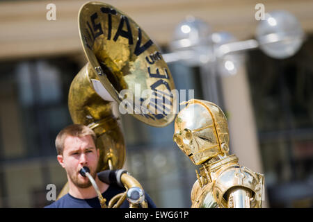 Cologne, Allemagne. 25 Juin, 2015. Musicien de rue Gustav fonctionne comme il est à côté d'une figure de cire de 'C-3PO' de la franchise Star Wars film en face de la cathédrale de Cologne, Allemagne, 25 juin 2015. Madame Tussauds Berlin a ouvert une exposition spéciale intitulée "La guerre des étoiles, en étroite collaboration avec Disney et Lucas Films et a lancé une tournée promotionnelle à travers Dresde, Munich, Stuttgart, Francfort, Cologne et Essen du 22 au 25 juin 2015. PHOTO : ROLF VENNENBERND/dpa/Alamy Live News Banque D'Images