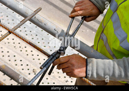 À l'aide de tenailles et travailleur sur le fil à lier ensemble des barres d'armature en acier pour béton armé pour Banque D'Images