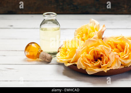 Parfum de rose dans une petite bouteille et la plaque en bois avec rose jaune fleurs sur fond blanc rustique Banque D'Images