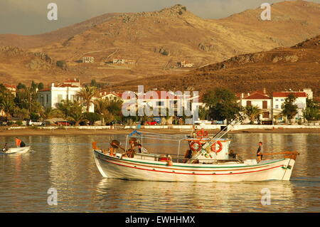 Bateau de pêcheur entre dans Myrina port de la ville au coucher du soleil. Tourkikos plage (baie) Maditos zone visible dans l'arrière-plan. Lemnos Limnos GR Banque D'Images