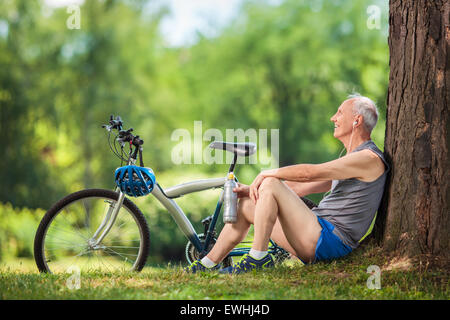 Senior man listening to music on headphones assis par un arbre dans un parc Banque D'Images