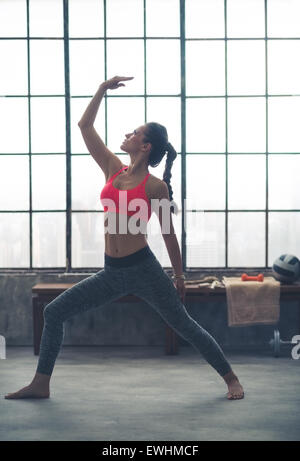 À la recherche jusqu'à sa main, une femme forte, s'étend dans une pose de yoga dans une salle de sport city loft. Banque D'Images