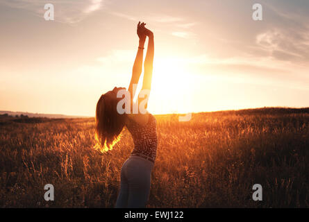 Free happy young woman raising arms au coucher du soleil dans le domaine en été. Contexte Banque D'Images