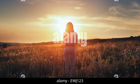 Free happy young woman raising arms au coucher du soleil dans le domaine en été. Contexte Banque D'Images