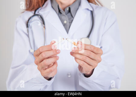 Femme médecin avec robe blanche et de casser un stéthoscope le tabac de cigarette dans ses mains sur fond blanc Banque D'Images