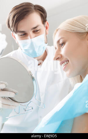 Smiling woman looking in mirror par dentiste Banque D'Images