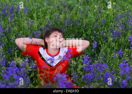 Teenage boy reposant sur la pelouse avec des fleurs bleu Banque D'Images