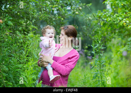 Jeune femme enceinte et sa petite fille de bébé la cueillette des pommes dans un jardin de fruits sur un jour d'automne froid et pluvieux Banque D'Images