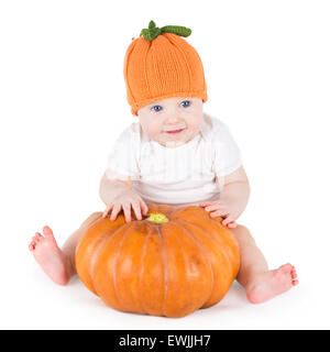 Funny rire petit bébé assis et jouant sur une énorme citrouille citrouille portant un chapeau tricoté sur fond blanc Banque D'Images