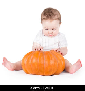 Funny rire petit bébé assis et jouant sur une énorme citrouille citrouille portant un chapeau tricoté sur fond blanc Banque D'Images