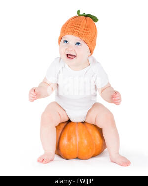 Funny rire petit bébé assis et jouant sur une énorme citrouille citrouille portant un chapeau tricoté sur fond blanc Banque D'Images