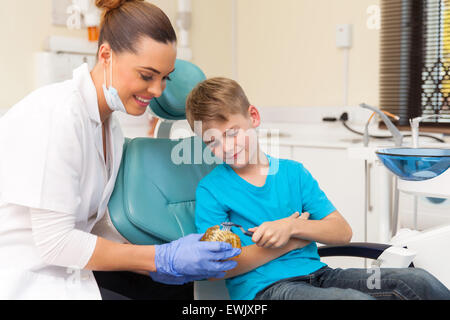 Friendly female dentist enseignement jeune garçon comment brosser les dents de son bureau Banque D'Images