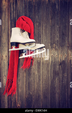 Vieux patins à glace avec un foulard rouge accroché sur la paroi en bois rustique Banque D'Images