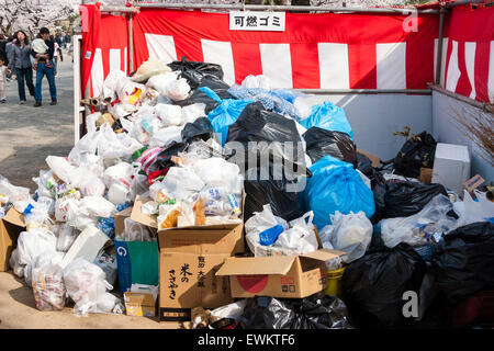 Pieux et des sacs en plastique remplis de détritus et d'ordures entassés autour de bac de litière après un après-midi de cherry blossom parties au parc du château de Himeji, Japon. Banque D'Images