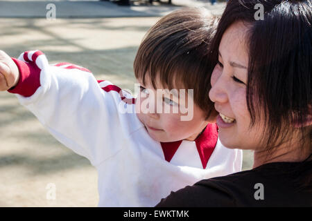 Gros plan de la tête et des épaules side view of young woman holding japonais enfant, garçon, de 3-4 ans à l'extérieur. C'est enfant du doigt quelque chose. Banque D'Images